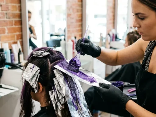Professional stylist applying purple pastel hair dye with brush onto foil-wrapped bleached hair sections