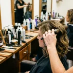 Hair stylist's hands working on a woman's wavy lob haircut at cluttered salon station with professional tools